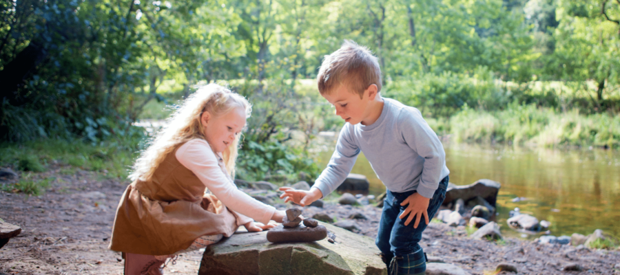 Two children stacking rocks on a large boulder by a stream